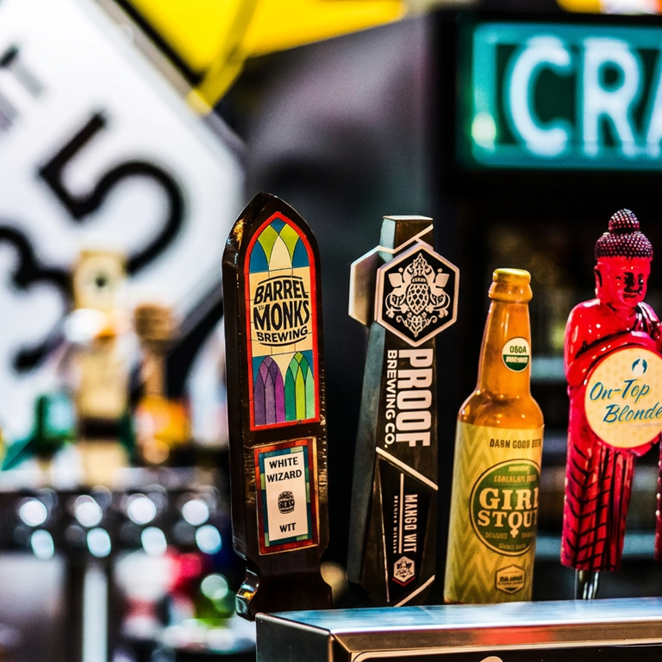 Craft beer taps and bottles, including Barrel Monks, Pieloft Brewing, Girl Stout, and HopGun, displayed at a bar.