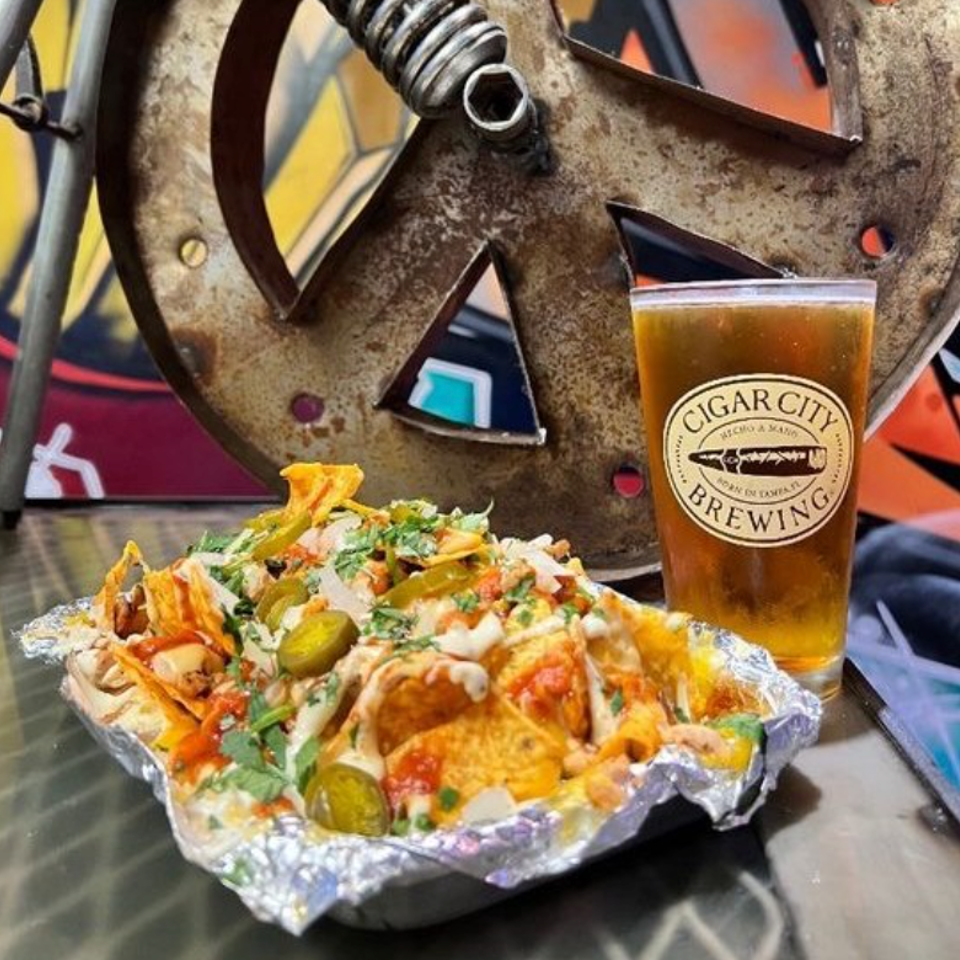 Loaded nachos with jalapeños beside a glass of craft beer.