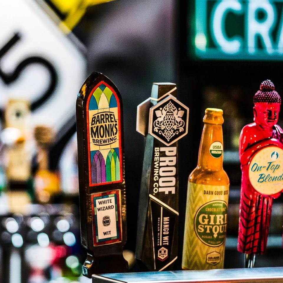 Craft beer display featuring colorful tap handles, a bottled Girly Stout, and red Buddha-shaped On-Top Blonde and Hop Gun taps.