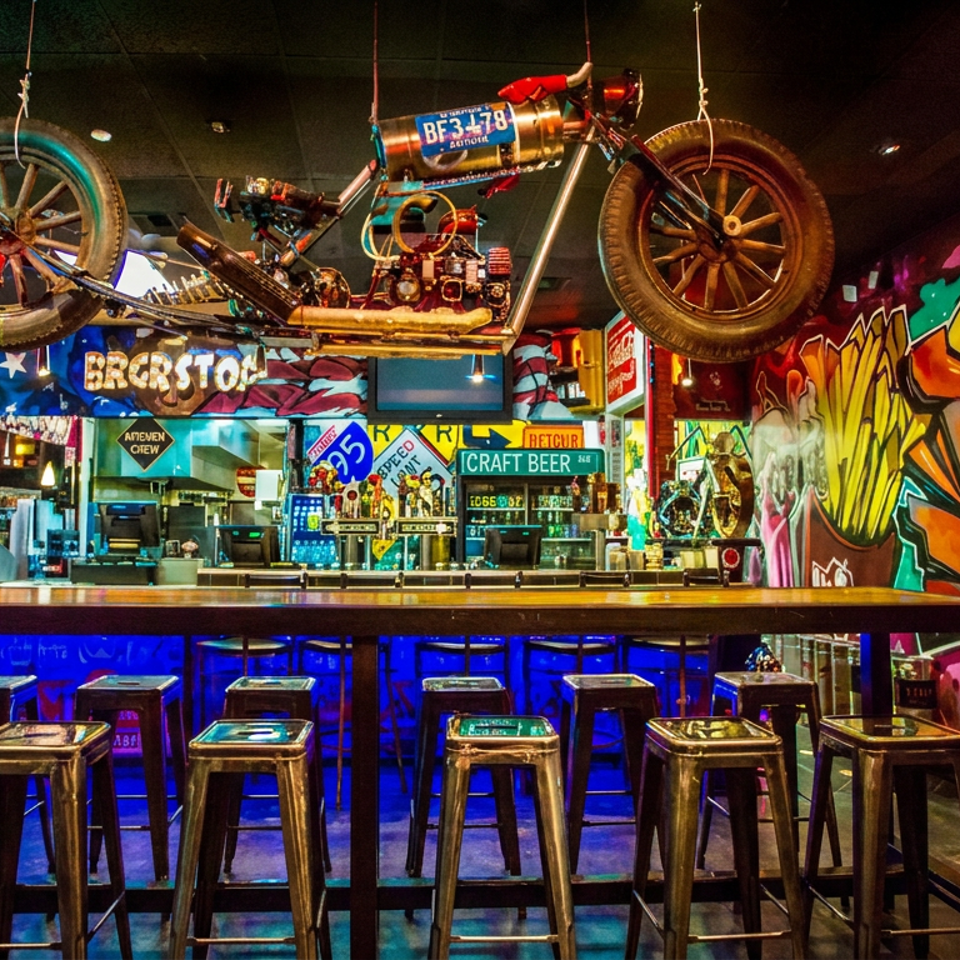 Vibrant graffiti-covered bar with blue lighting, stools, craft beer taps, and a motorcycle mounted above the counter.