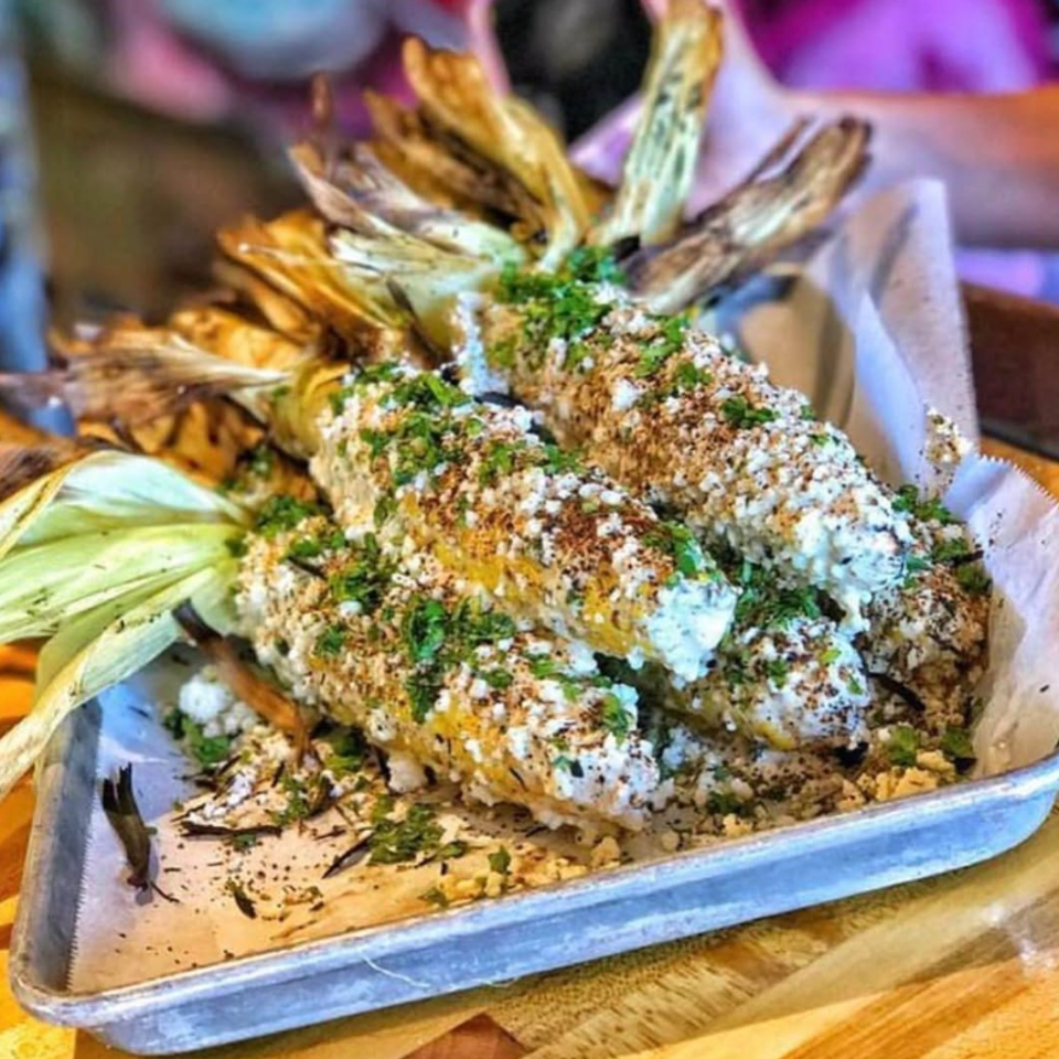 Grilled corn topped with creamy sauce, crumbled cheese, and herbs.