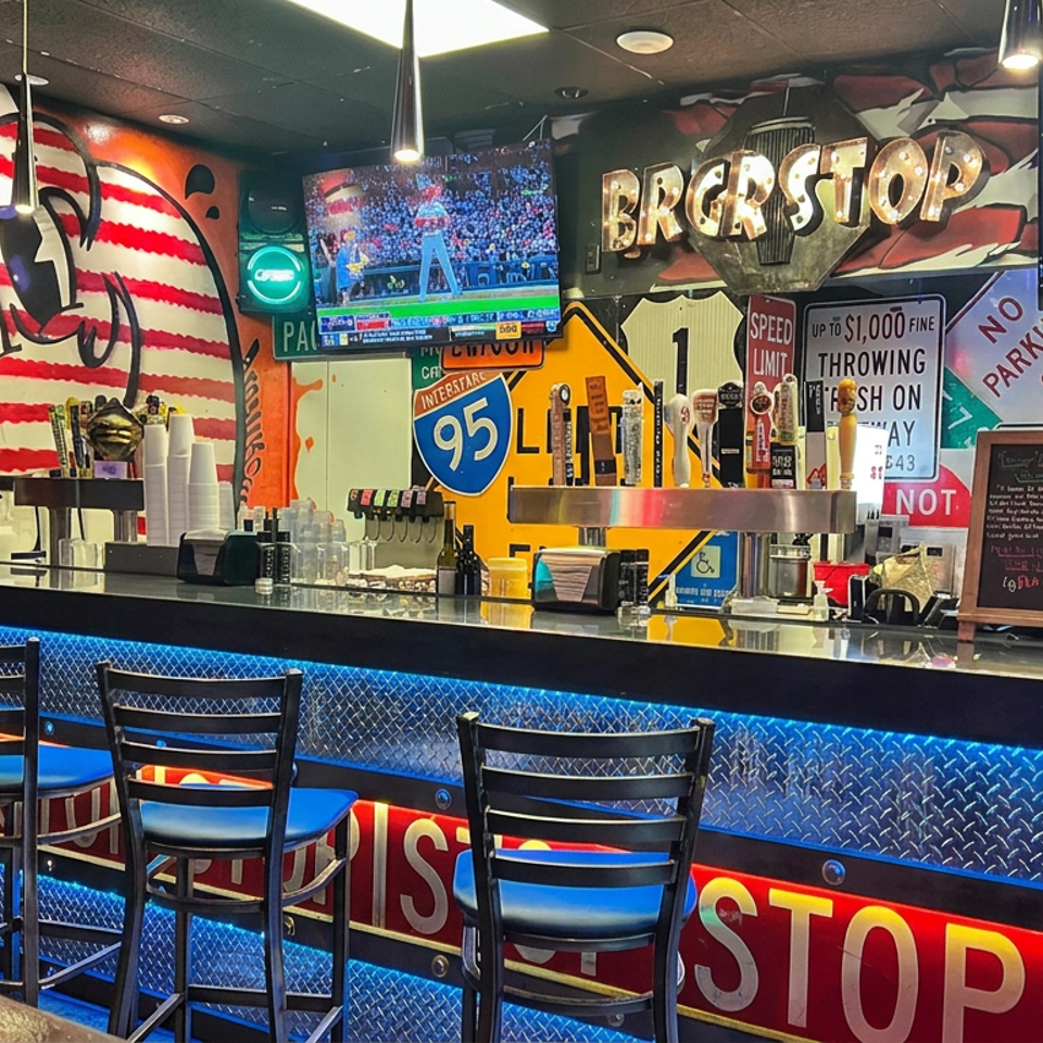 Sports bar interior with a blue-lit counter, high chairs, beer taps, televisions, and colorful American road-sign décor.