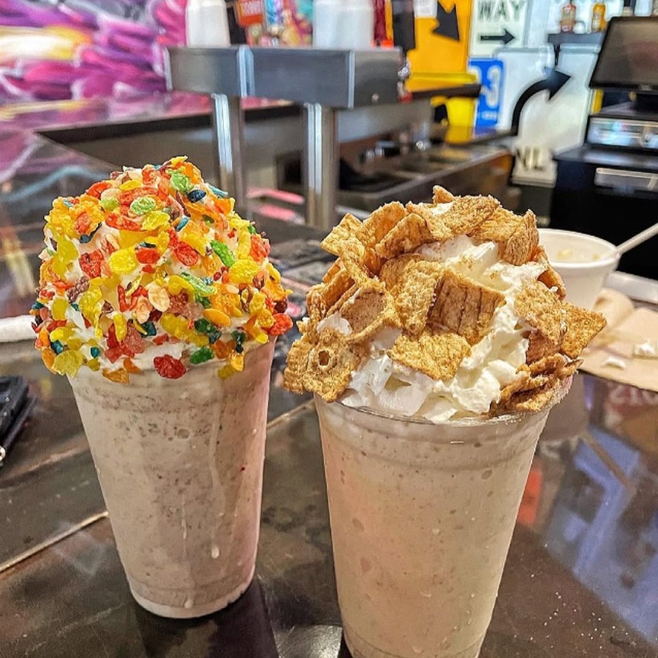Two craft milkshakes topped with whipped cream and colorful cereal.